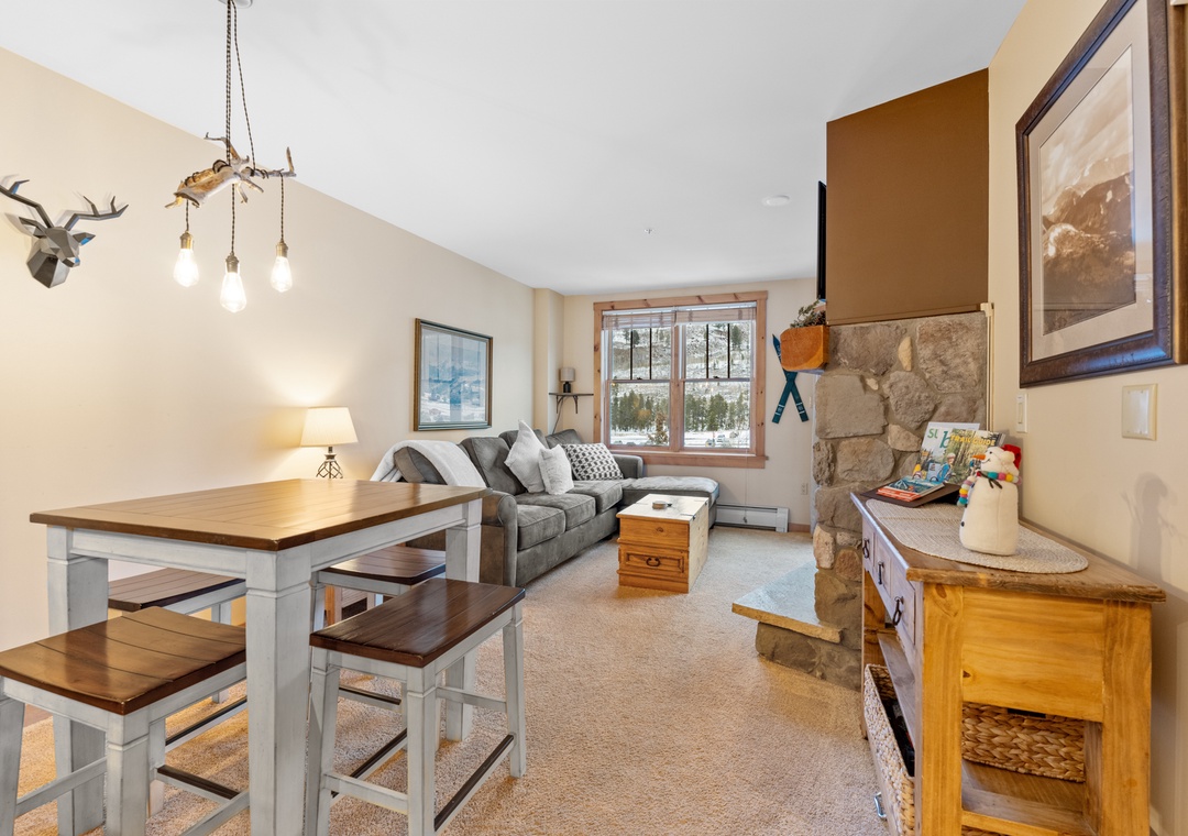 Cozy up in your rustic living space with stone fireplace, comfy seating, and mountain views through large windows.