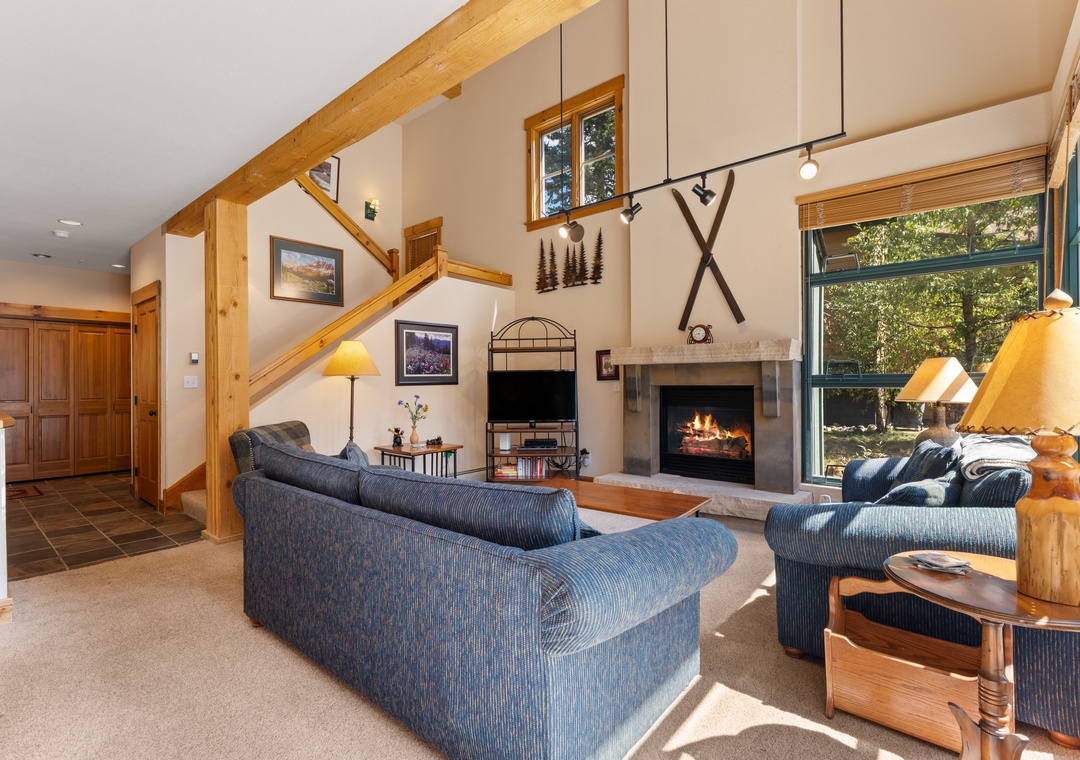 Unwind in your cozy living room with vaulted ceilings, rustic wood beams, and a warm stone fireplace. Large windows frame beautiful forest views while comfortable seating invites you to relax after your mountain adventures.