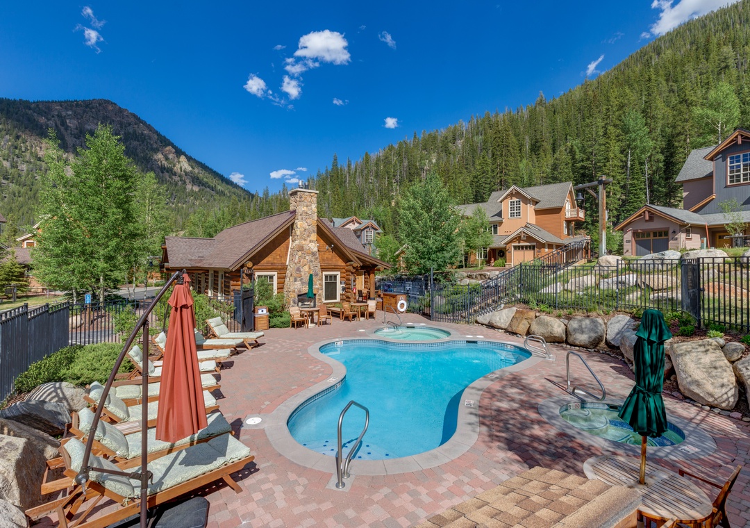 A mountain-framed outdoor pool and hot tub area surrounded by pine forests, offering peaceful alpine scenery and relaxation at this vacation retreat.