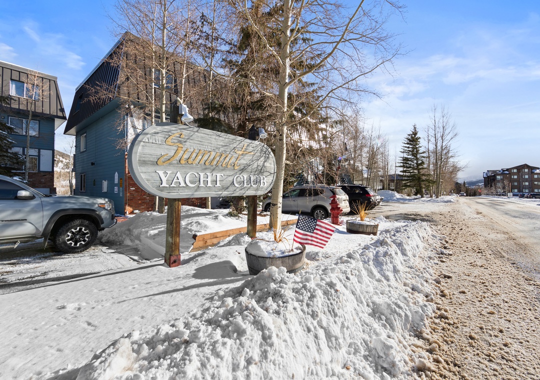 The Yacht Club entrance welcomes visitors with its distinctive signage amid a snowy mountain setting, marking your arrival at this winter retreat.