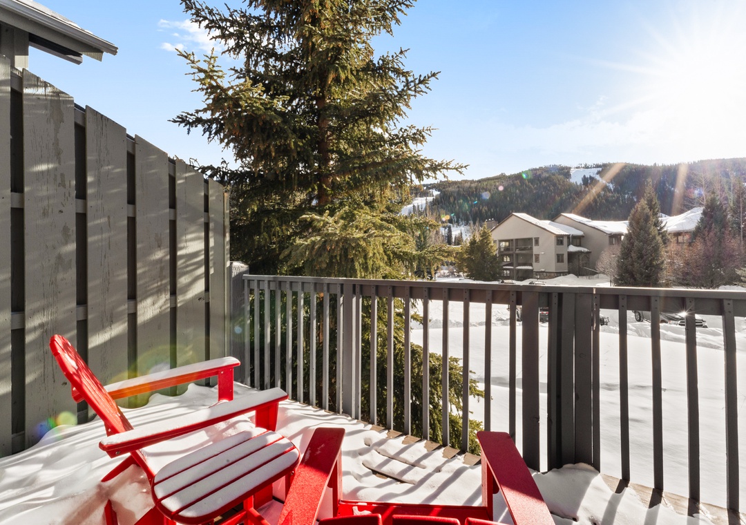 Relax on your private balcony with stunning mountain views, where red Adirondack chairs invite peaceful moments overlooking the snowy alpine landscape.