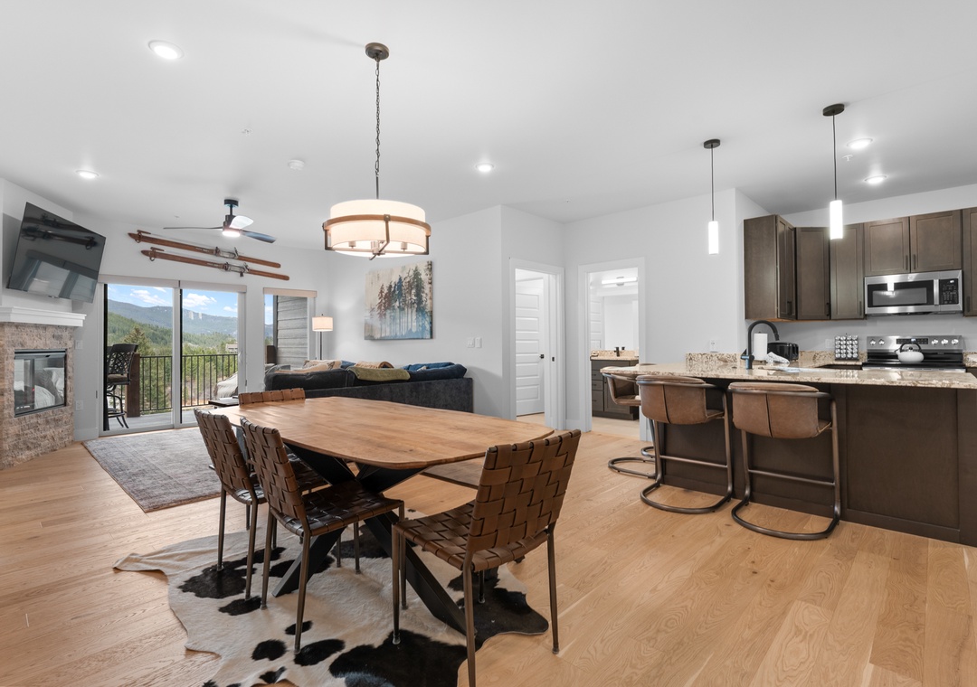 Your open-concept retreat blends mountain-modern elegance with cozy warmth, featuring a spacious dining table, a chef's kitchen, and stunning forest views beyond.