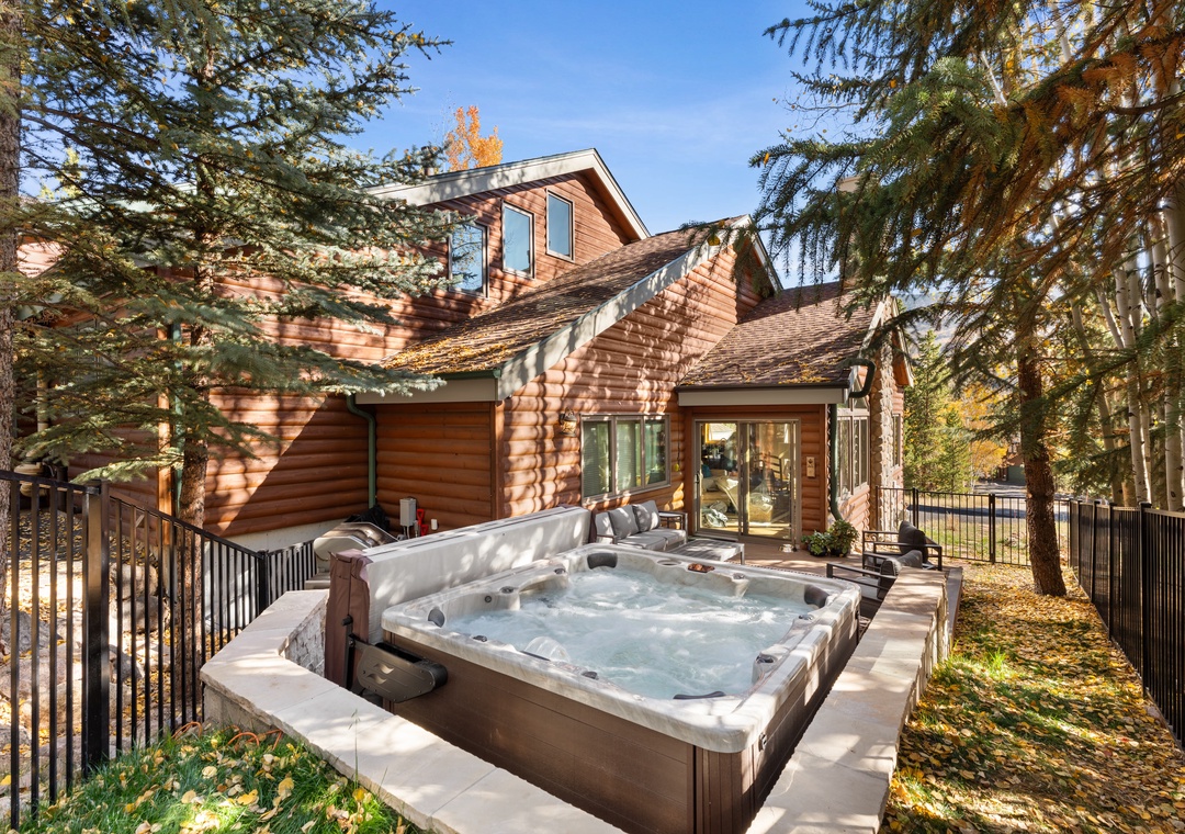 Charming mountain retreat with warm wood siding and private hot tub on the deck, surrounded by evergreens and autumn foliage. A peaceful, secluded setting for relaxation.