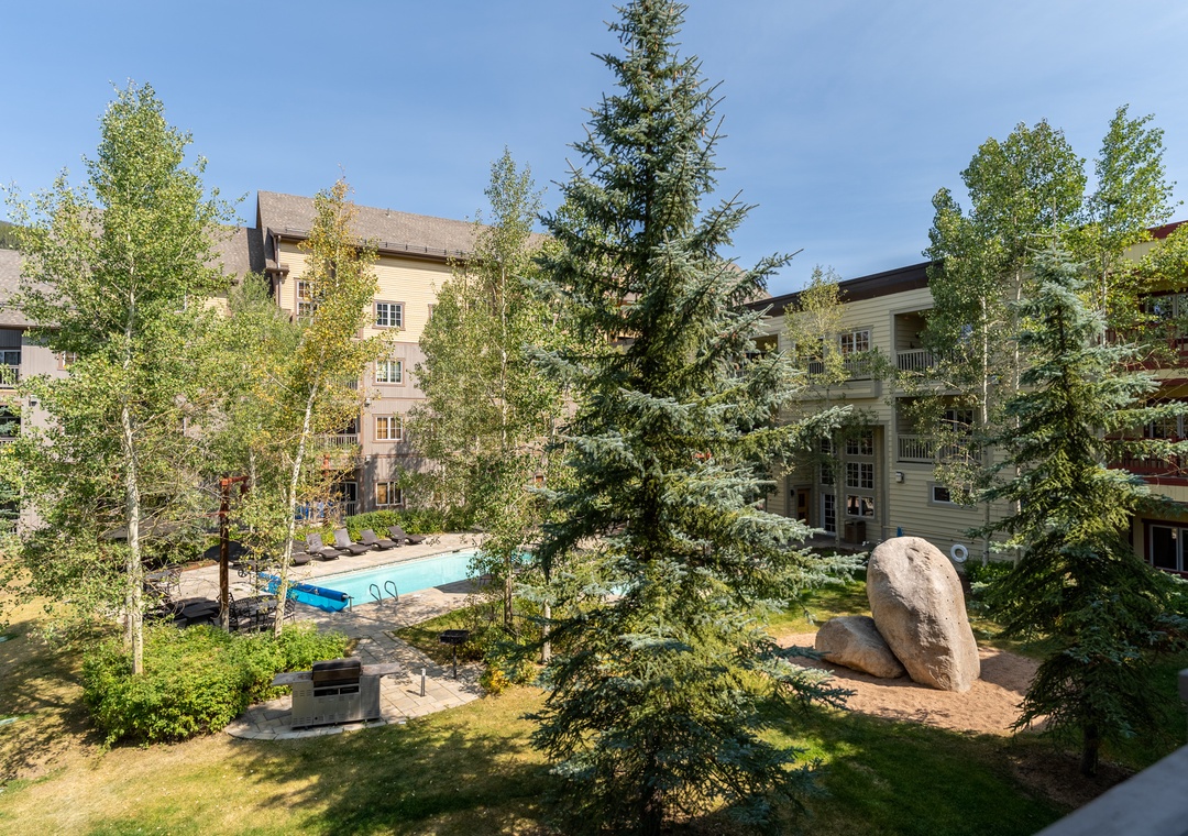 Serene resort complex featuring swimming pool, lush gardens, and multi-story accommodations surrounded by towering evergreens and manicured landscaping.
