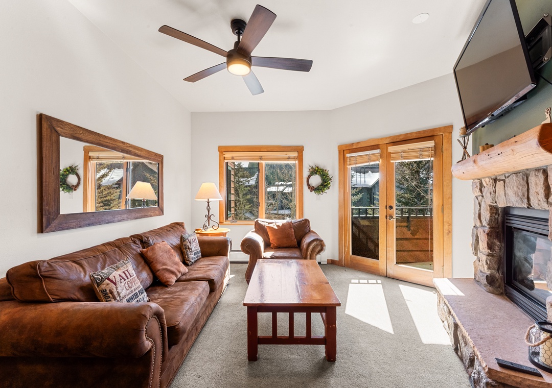 Unwind in your cozy living room with rich leather seating, crackling stone fireplace, and mountain views through expansive windows.