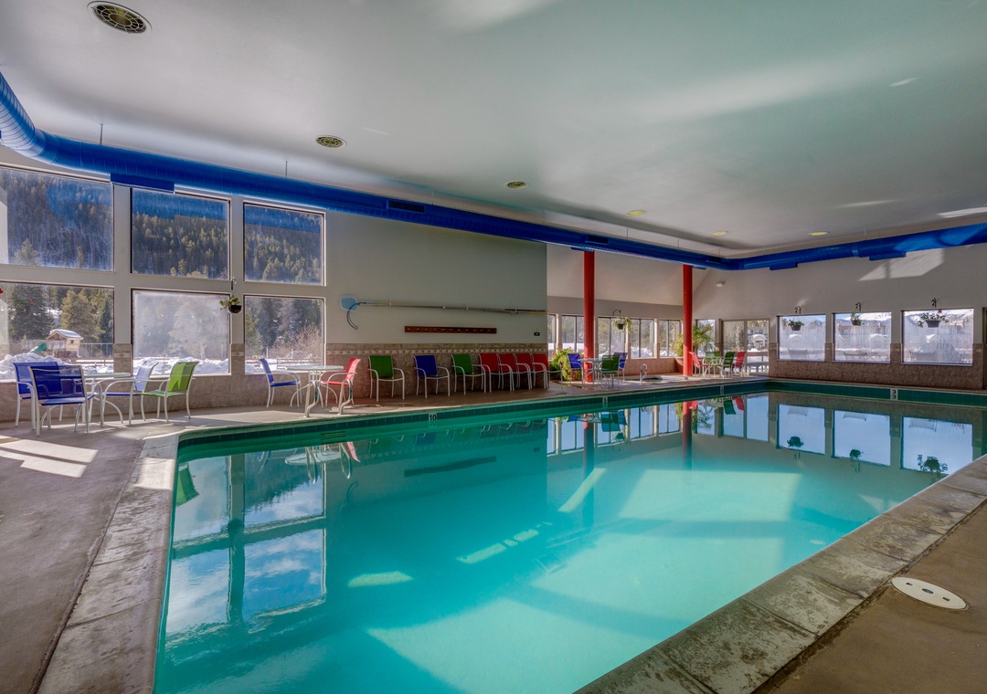 Dive into your private indoor pool with mountain views through floor-to-ceiling windows, surrounded by colorful seating areas perfect for relaxation.