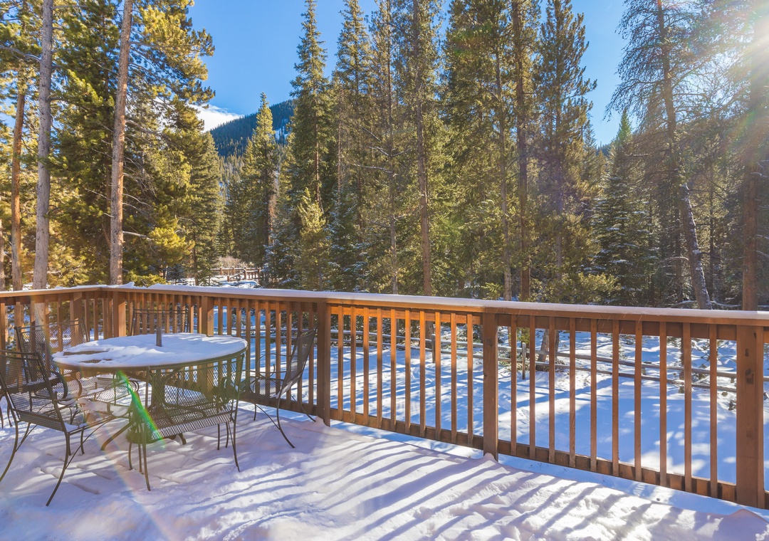 Snow-covered deck with forest and mountain views creates a peaceful winter retreat for morning coffee or evening relaxation.