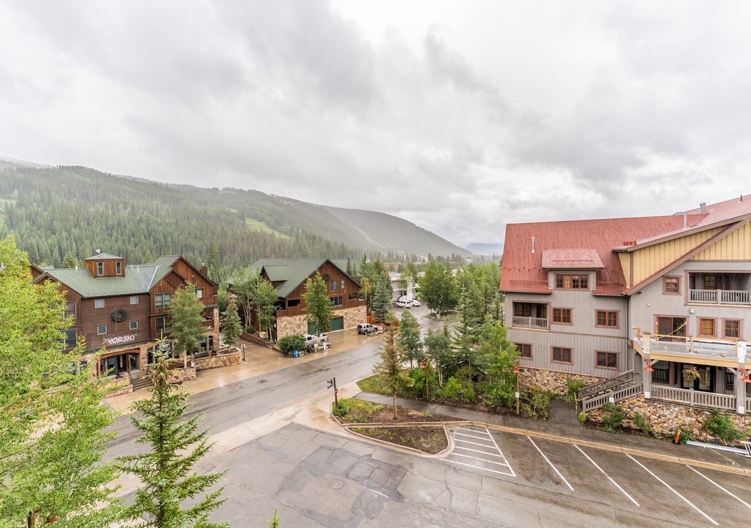 Mountain resort area with forested hills, lodge-style buildings, and easy parking access.