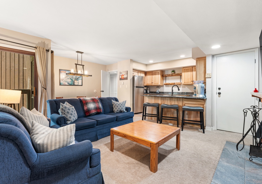 Settle into your inviting living space where a plush blue sofa and cozy armchair await your arrival, seamlessly flowing into a fully-equipped kitchen with breakfast bar seating for easy meals and conversation.