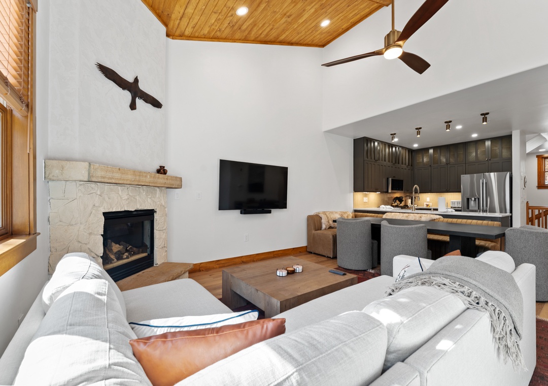 Relax in your open-concept living space featuring a cozy stone fireplace, modern kitchen, and comfortable seating perfect for mountain evenings.