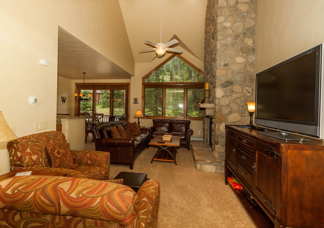 Cozy up in this warm living space with leather seating, stone fireplace, and forest views through expansive windows.
