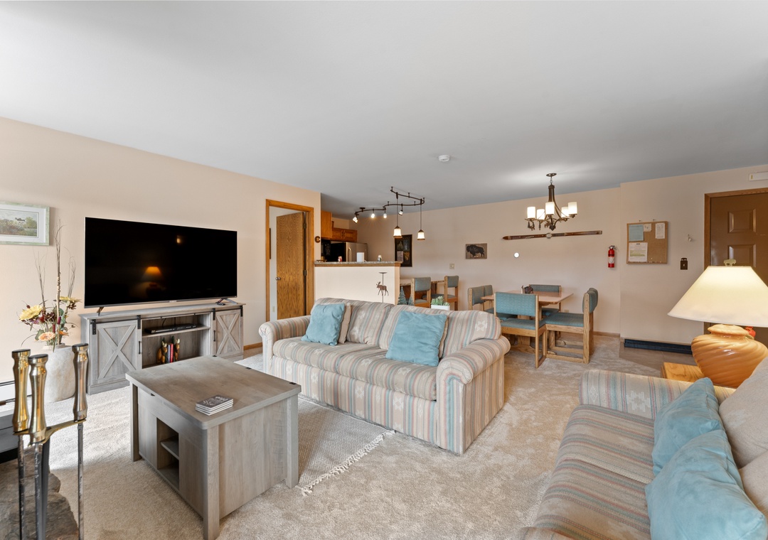 Settle into your spacious living room featuring plush striped sofas, a large flat-screen TV, and an open layout that flows seamlessly into the dining area.