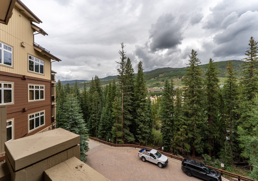 Mountain views stretch beyond tall evergreens from this elevated property, with nearby parking visible in the foreground.