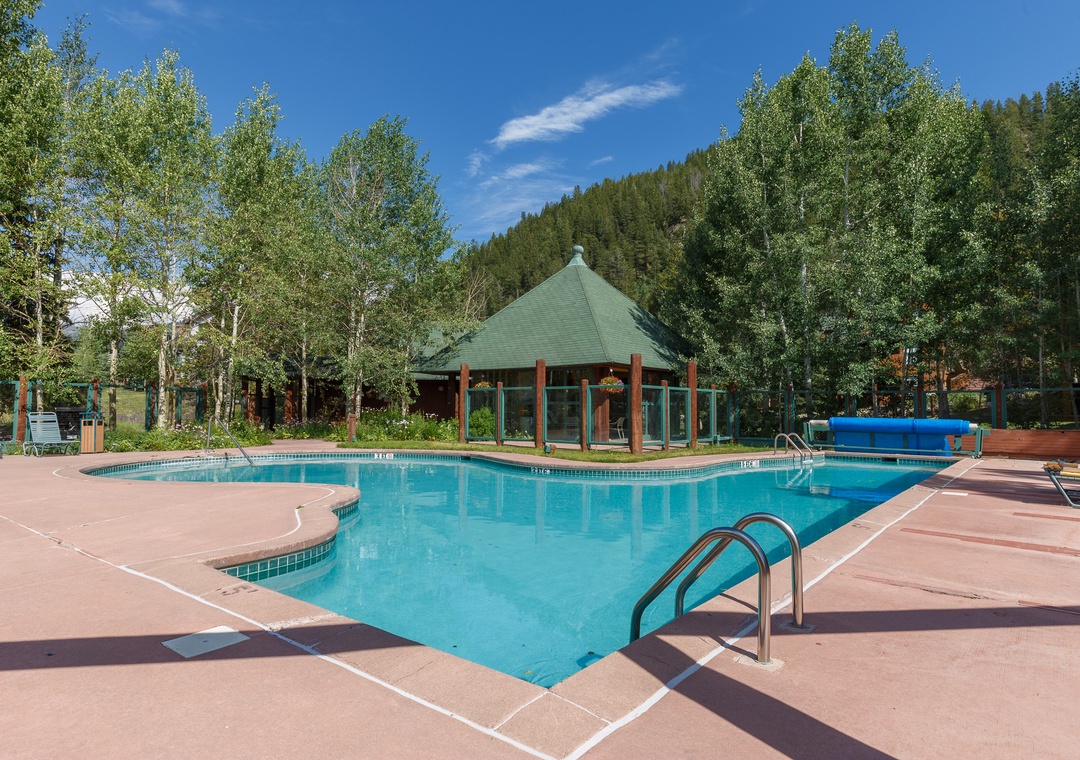 Resort-style pool surrounded by mature trees and mountain views, creating a peaceful alpine retreat setting.