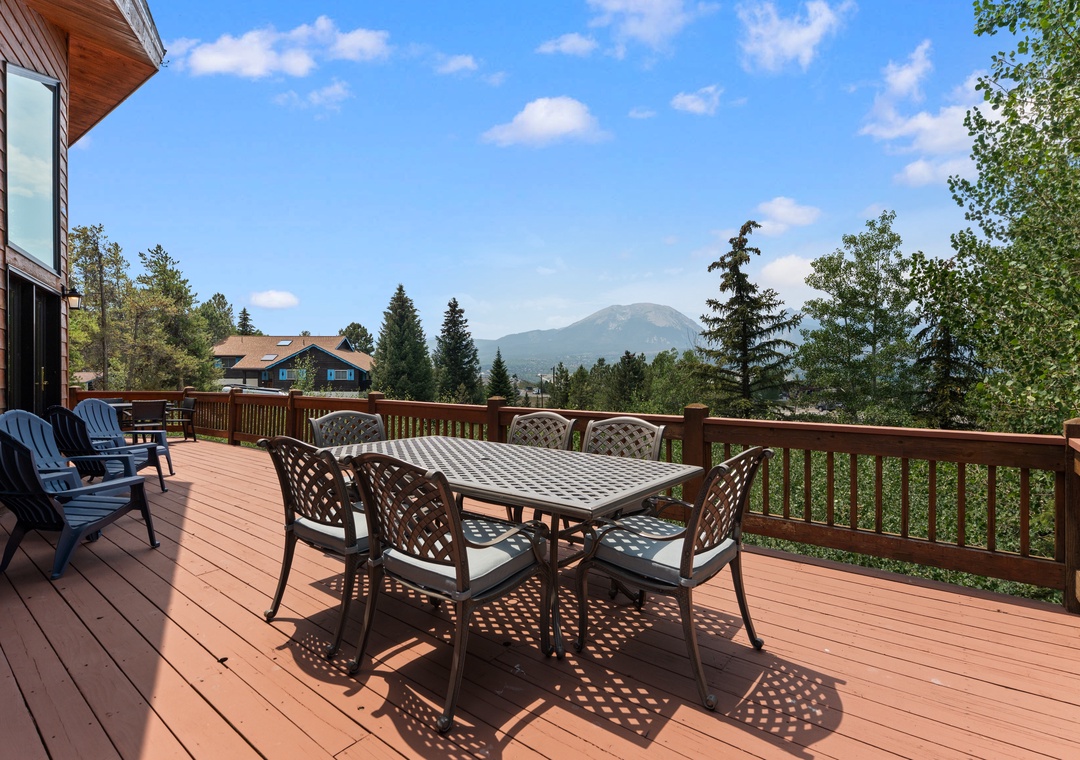 A spacious deck offering mountain vistas and scenic views of the surrounding neighborhood. Outdoor dining and lounge seating provide a peaceful setting for taking in the natural landscape.