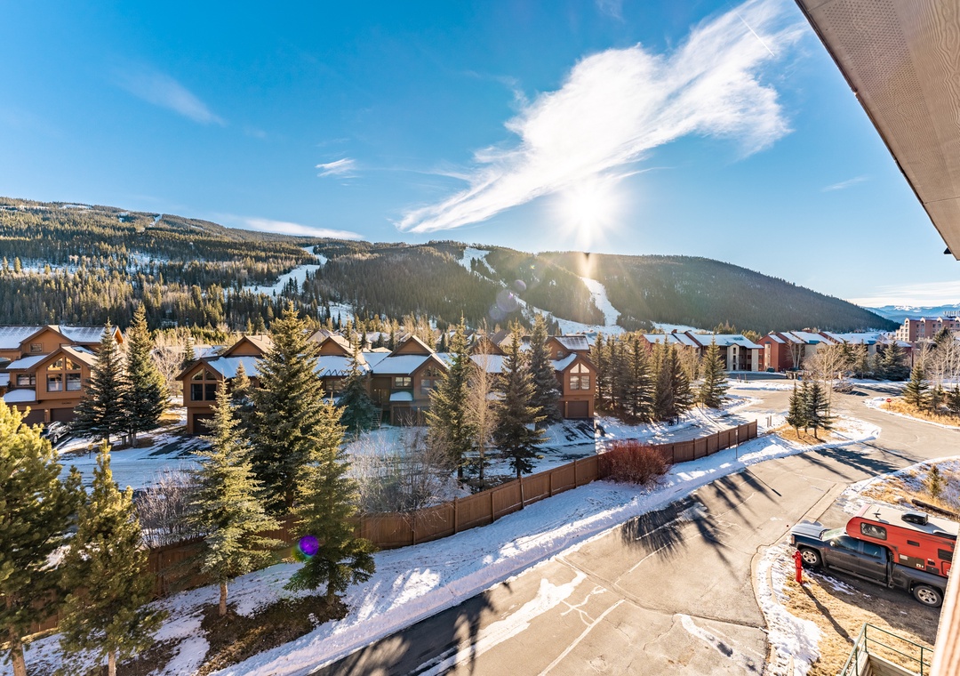 Mountain resort community with ski slopes visible across snow-covered landscape and residential chalets nestled among evergreen trees.