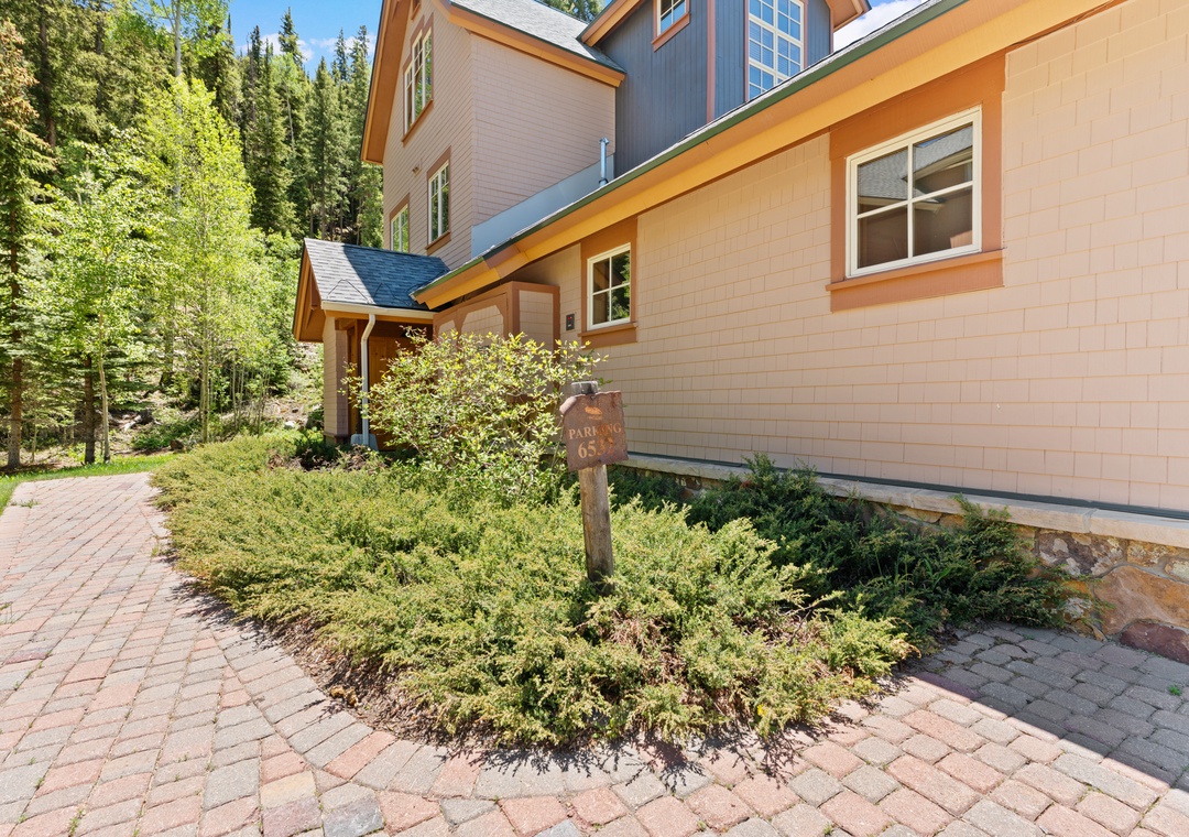 A welcoming mountain retreat nestled among towering pines, with a charming paver walkway leading to your private entrance, surrounded by natural landscaping and alpine tranquility.