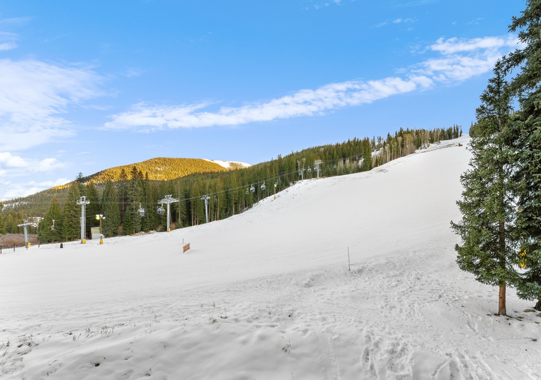 Snow-covered ski slopes with chairlifts ascending through forested mountains under clear winter skies.