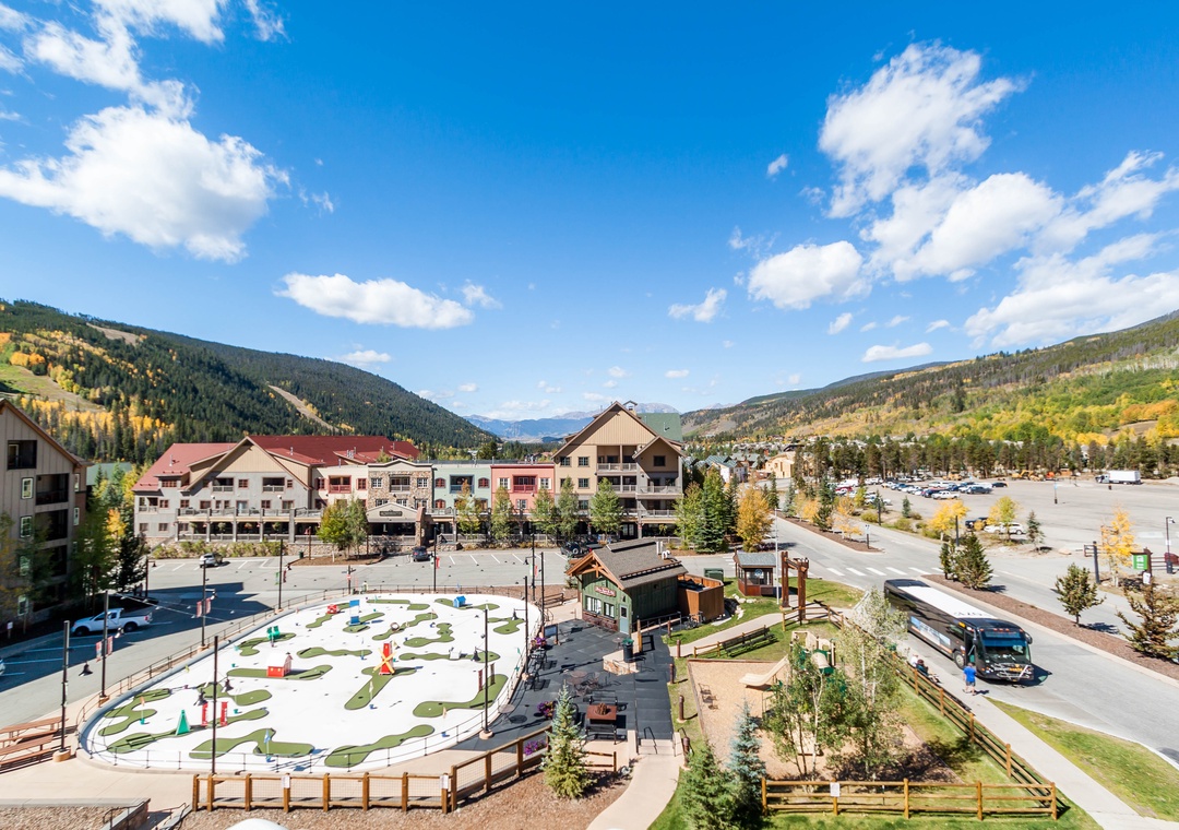 Mountain resort village with autumn foliage, recreational facilities, and scenic alpine valley backdrop during a perfect day.