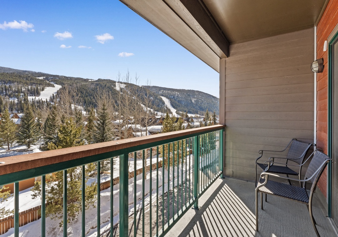 This balcony frames sweeping views of snow-dusted ski slopes and forested mountains. Two chairs invite quiet moments amid fresh alpine air and sunlit winter scenery.