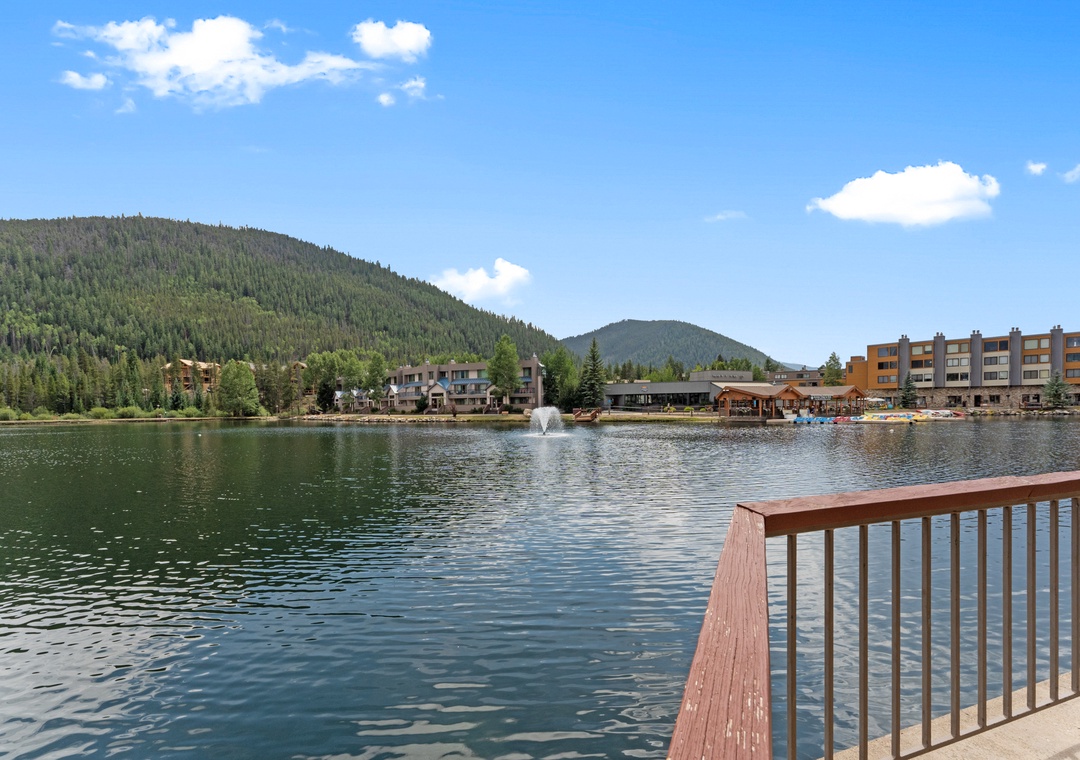 Pristine mountain lake surrounded by forested peaks and waterfront resort buildings under blue skies.