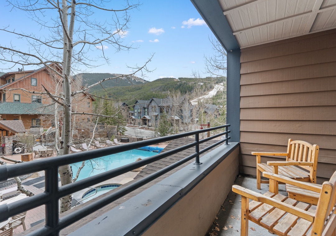 This balcony overlooks mountain peaks and a sparkling pool below, offering a peaceful retreat where you can unwind in cozy wooden chairs and breathe in the fresh alpine air.