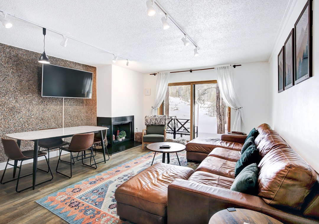 Unwind in your stylish living space with rich leather seating, modern fireplace, and snowy mountain views through large windows.