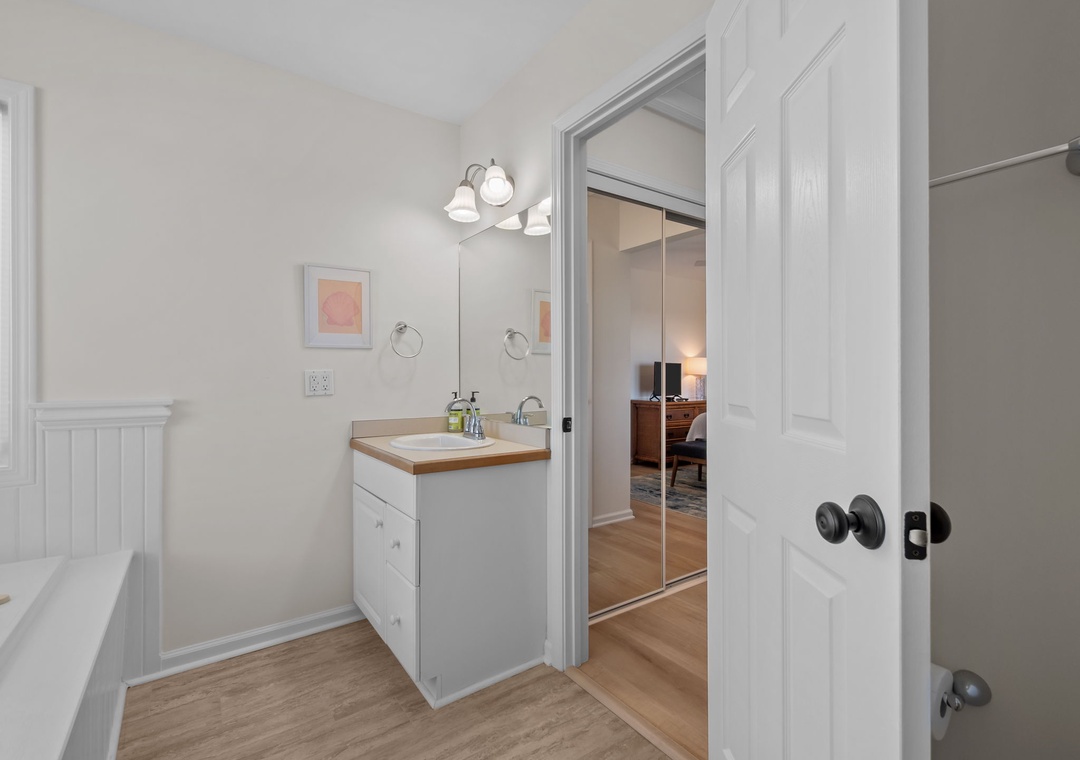 Your bright bathroom features clean white cabinetry, warm wood-look floors, and thoughtful details like framed art to make your daily routine feel special.