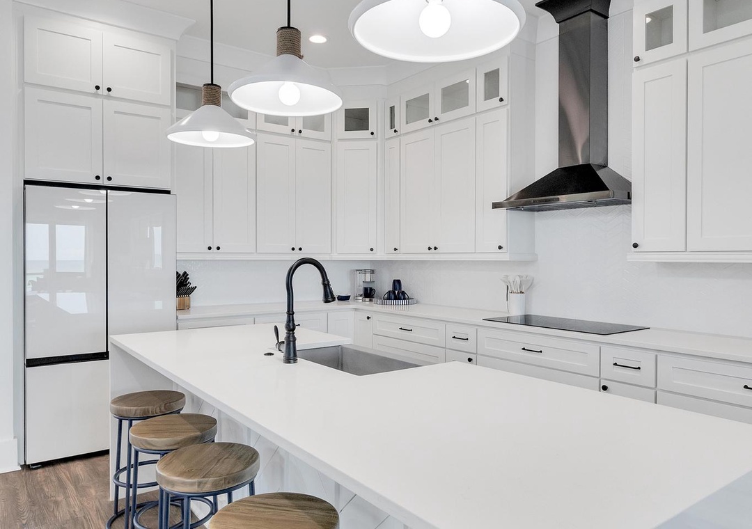 A bright, modern kitchen featuring white cabinetry, sleek pendant lighting, and a spacious island with bar seating—perfect for gathering and meal prep during your stay.