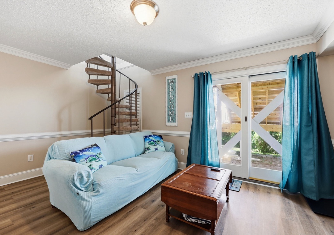 Unwind on your cozy sofa while natural light pours through glass doors, revealing a charming porch view. A spiral staircase adds character, inviting you to explore upstairs.