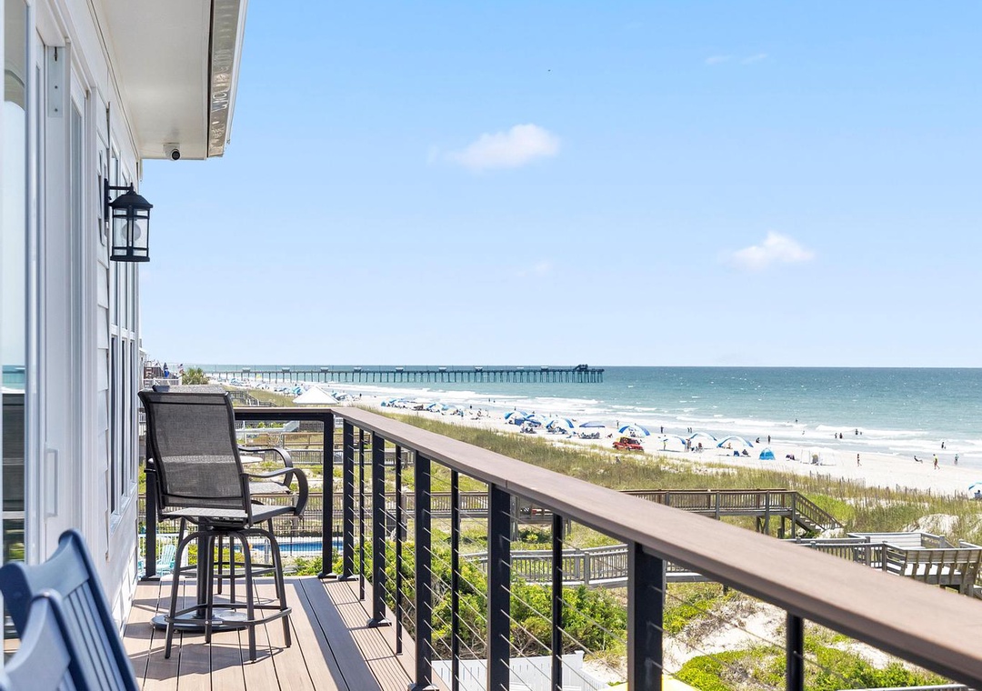 The property's beachfront deck offers elevated views of the sandy shore, coastal dunes, and ocean pier, providing guests a serene vantage point for relaxing above the beach.