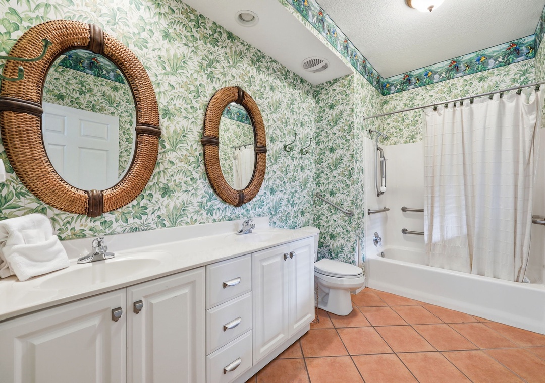 A bright bathroom featuring botanical wallpaper, dual wicker-framed mirrors, white vanity, and a tub-shower combo for your comfort.