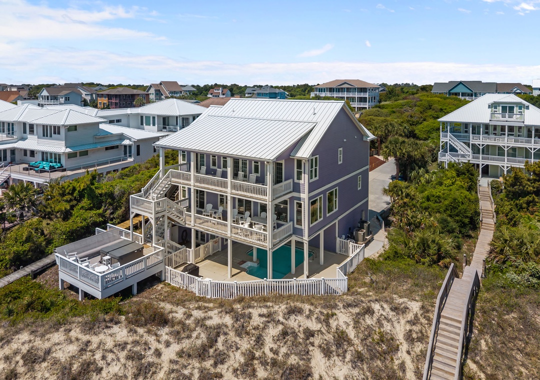 Elevated coastal home with private pool and decking, nestled among lush vegetation with beach boardwalk access.