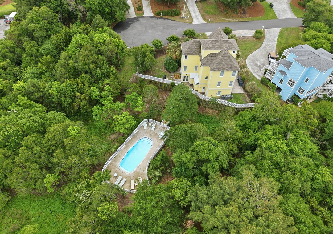 Aerial view showcasing the property and its inviting pool area, set within lush natural surroundings and a quiet residential neighborhood.