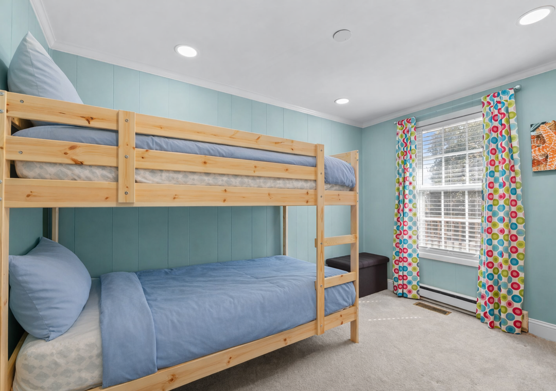 Rest peacefully in your cozy bunk bed bedroom with cheerful blue walls and bright colorful curtains creating the perfect family-friendly retreat.