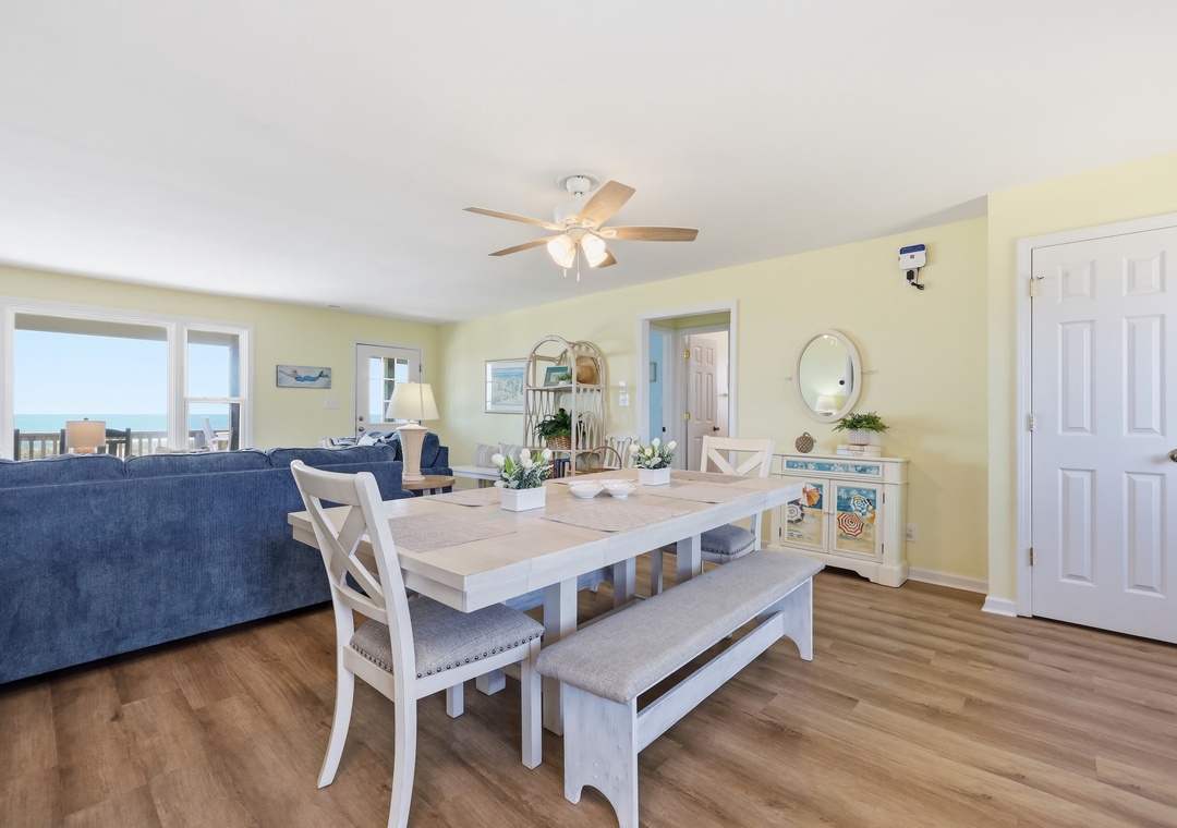 Step into your airy beach retreat where sunny yellow walls and coastal charm set the tone. Large windows frame stunning ocean views, perfect for morning coffee at your dining table or relaxing on the plush blue sofa.