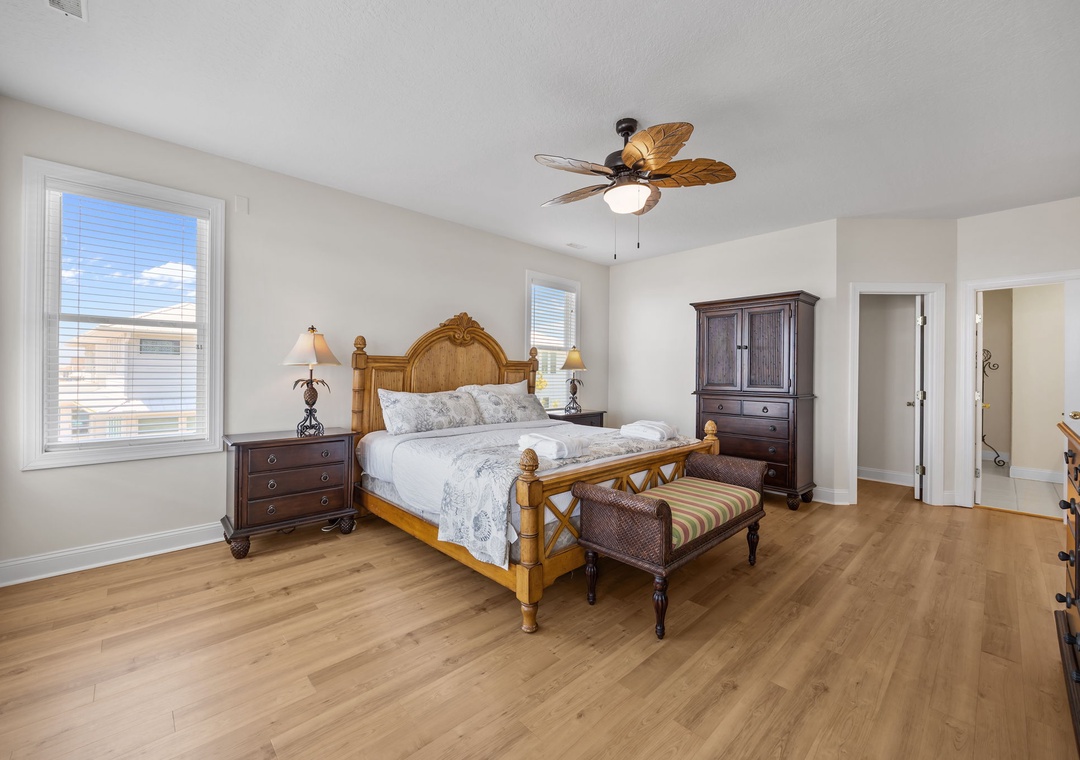 Relax in your spacious bedroom with warm wood floors, tropical ceiling fan, and elegant furnishings for a perfect coastal retreat.