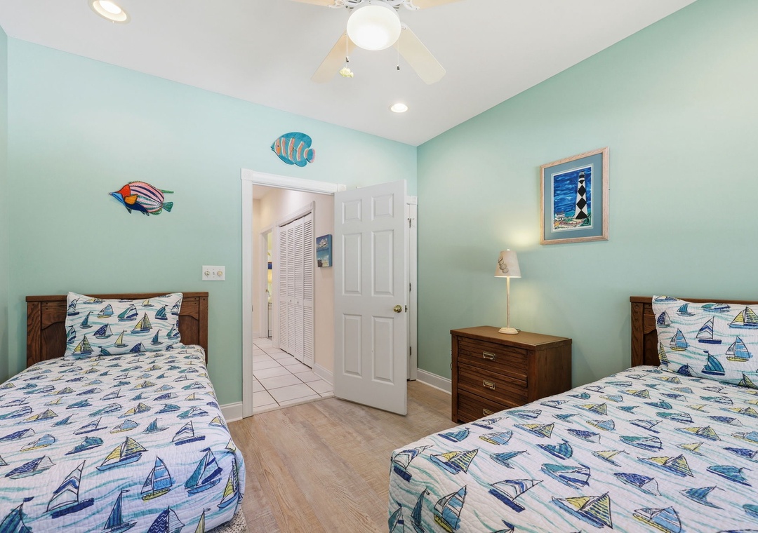 Drift off to sleep in this cheerful coastal-themed bedroom with two cozy twin beds, playful sailboat linens, and whimsical fish art creating a serene seaside escape.