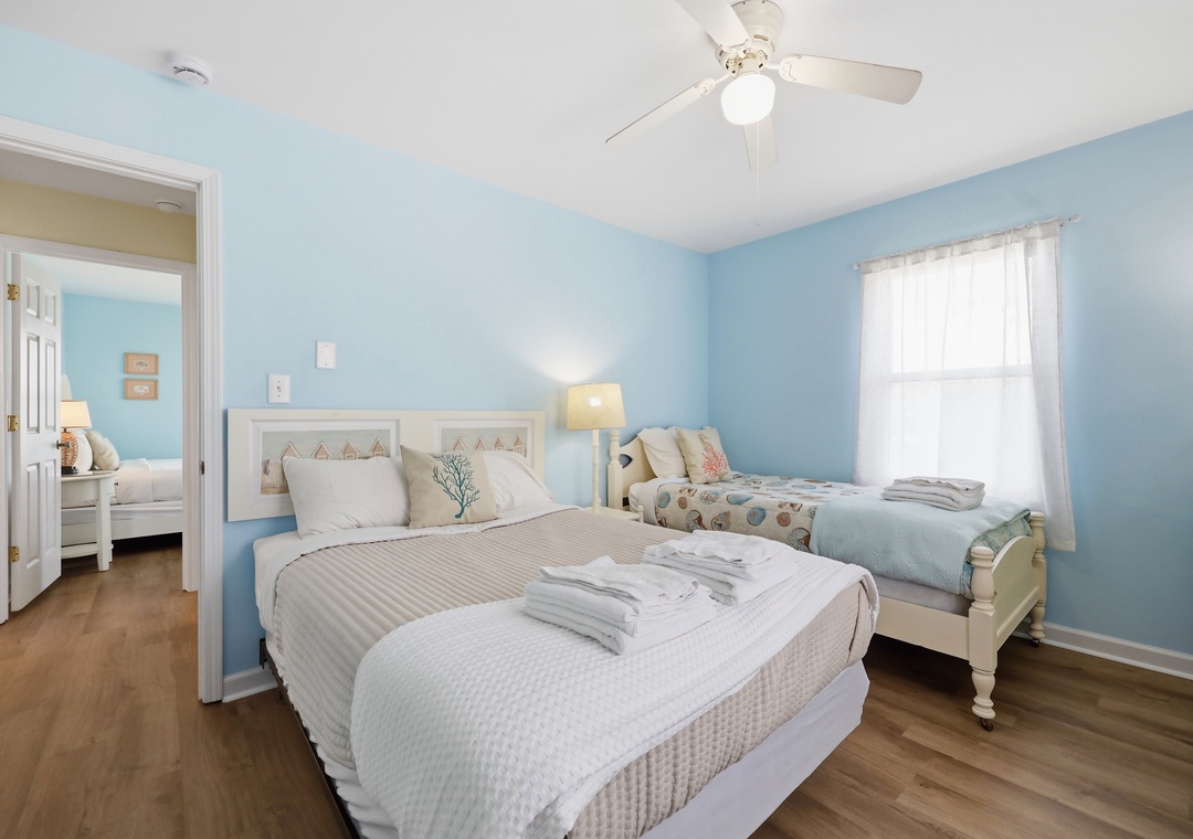 You'll love the calming coastal vibe of this airy bedroom, with soft blue walls, comfortable beds dressed in fresh linens, and a gentle breeze from the ceiling fan above.