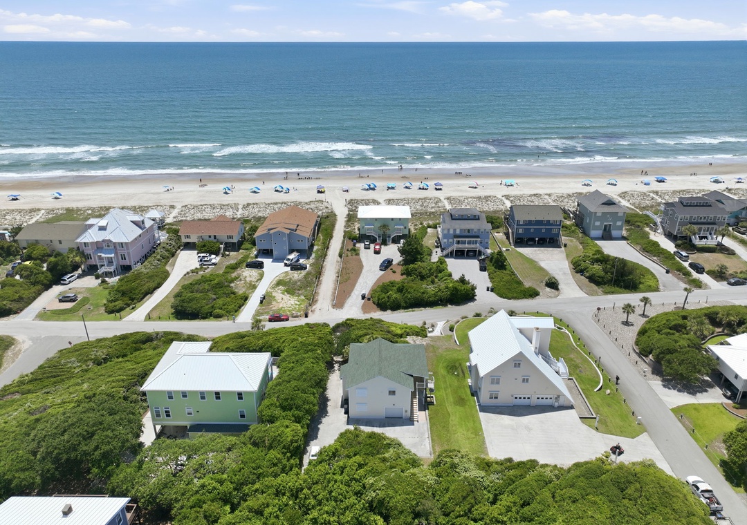 Aerial view showcasing beachfront vacation homes nestled along pristine sandy shores, with direct beach access and stunning ocean vistas stretching to the horizon.