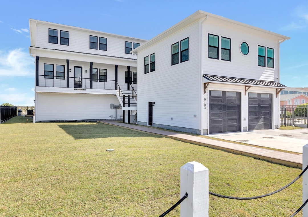 This modern coastal home features clean white siding, spacious covered decks, and a generous two-car garage, providing a bright and welcoming arrival experience for guests.