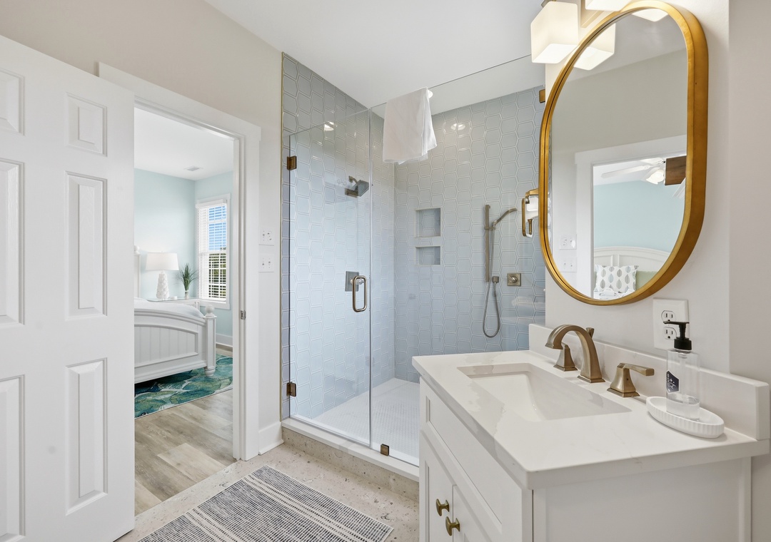 Unwind in your elegant bathroom with a spa-like rainfall shower, chic gold fixtures, and calming coastal hues that invite pure relaxation.