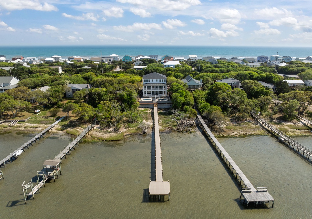 Elevated coastal property with private dock extending into calm waters, surrounded by mature trees and beachfront community.