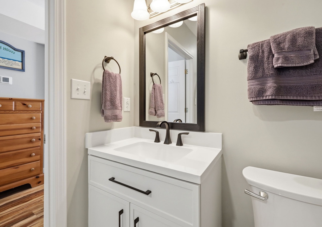 Freshen up in this bright, welcoming bathroom with soft purple towels, modern fixtures, and a clean vanity—your perfect retreat after a beach day.