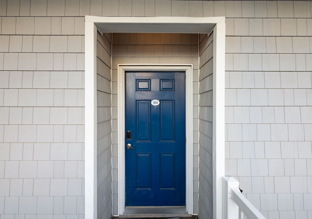 Classic coastal-style entrance featuring a striking blue door and weathered shingle siding that welcomes guests to unit 404.