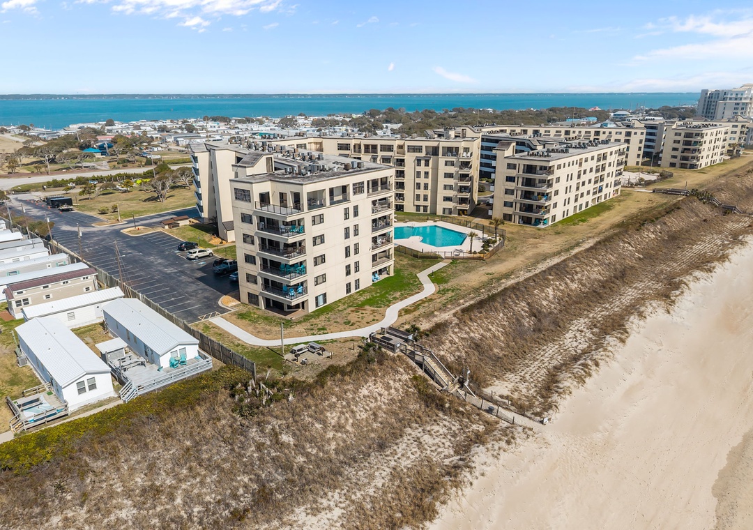 Beachfront property situated directly on sandy shores with pool access, neighboring residential areas, and scenic coastal water views.