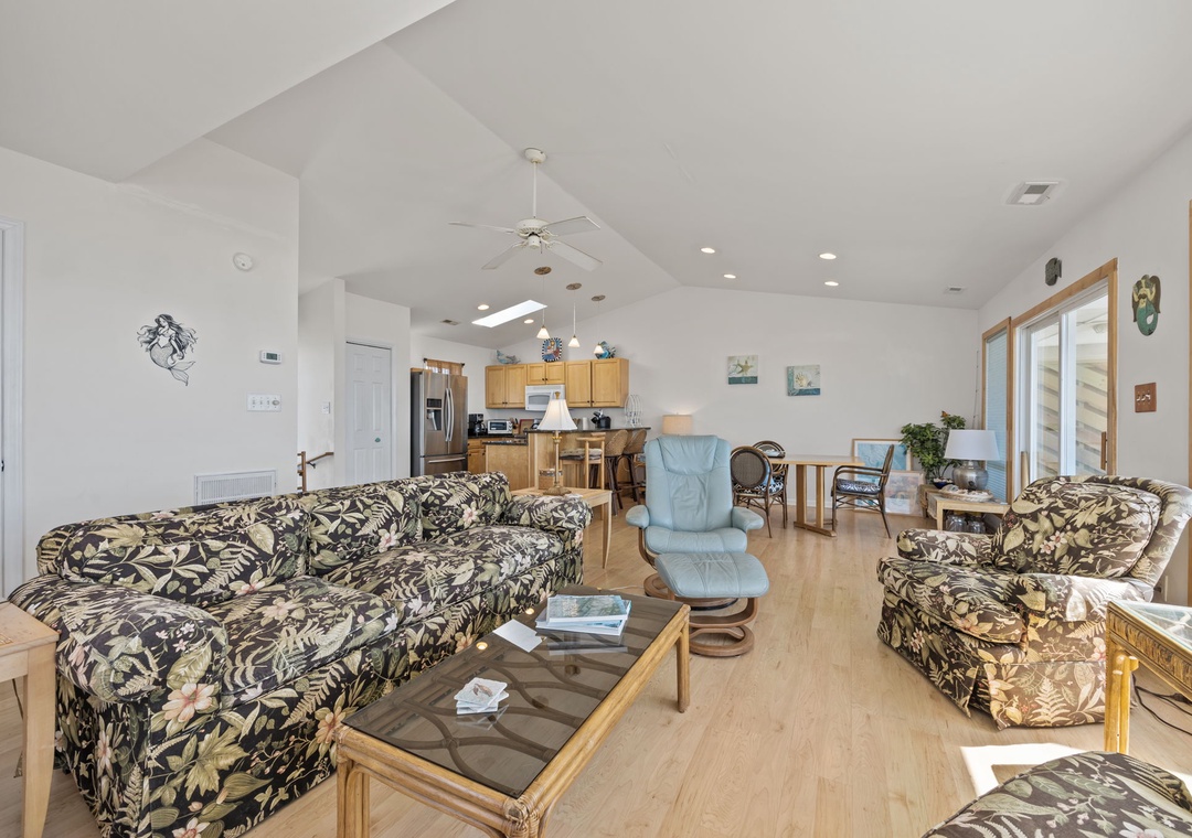 Relax in your spacious open-concept living area with tropical-print seating, modern kitchen, and bright dining space perfect for gathering.