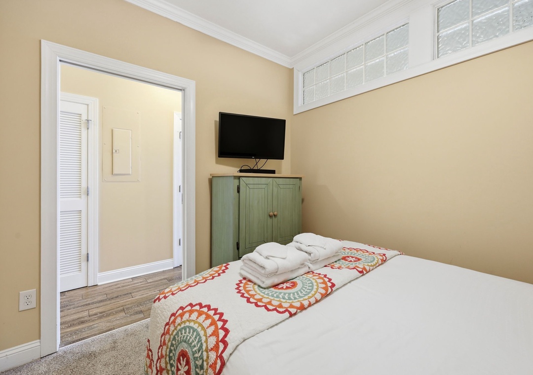 Your sunny bedroom features a cozy bed dressed in cheerful linens, with a flat-screen TV for your entertainment and a vintage-style cabinet for your belongings.