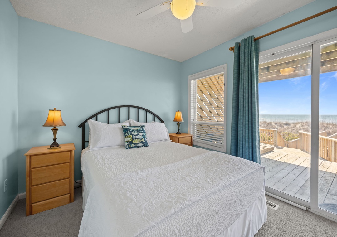 Wake up to ocean views through your private balcony doors in this serene coastal bedroom.