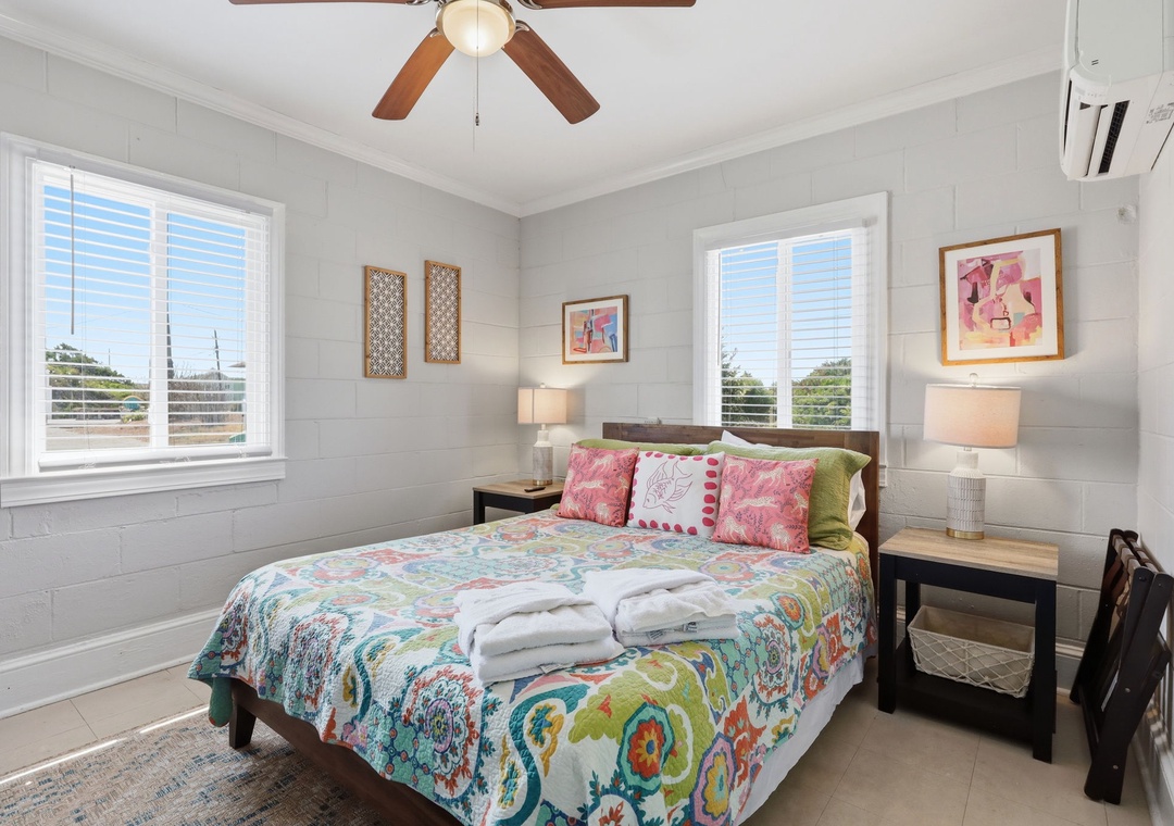 Step into your bright, airy bedroom where white shiplap walls and cheerful linens create a coastal sanctuary. Fresh towels await your arrival, while the ceiling fan and AC keep you cool as you unwind.